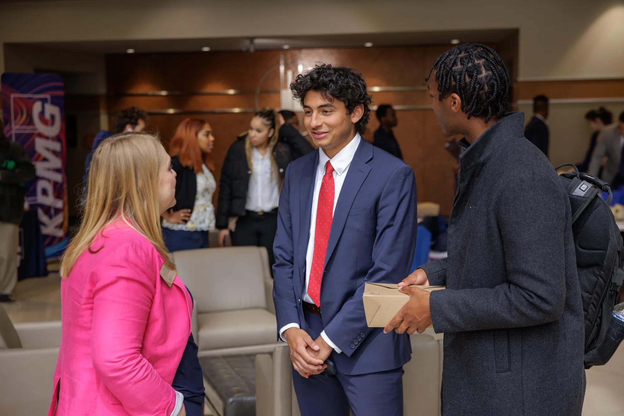 Two male students dressed in business professional attire talk with Kristen Collett-Schmitt during a networking and lunch event following the presentations. | Photo by Peter Ringenberg/University of Notre Dame