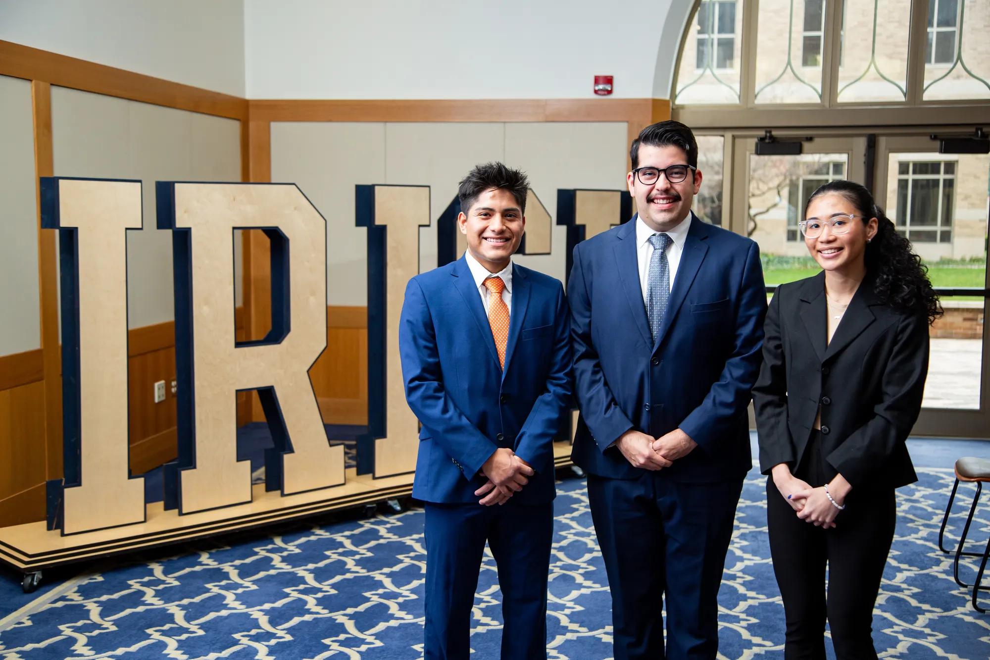 One team of two male students and one female student pose for a photo in business professional suits.