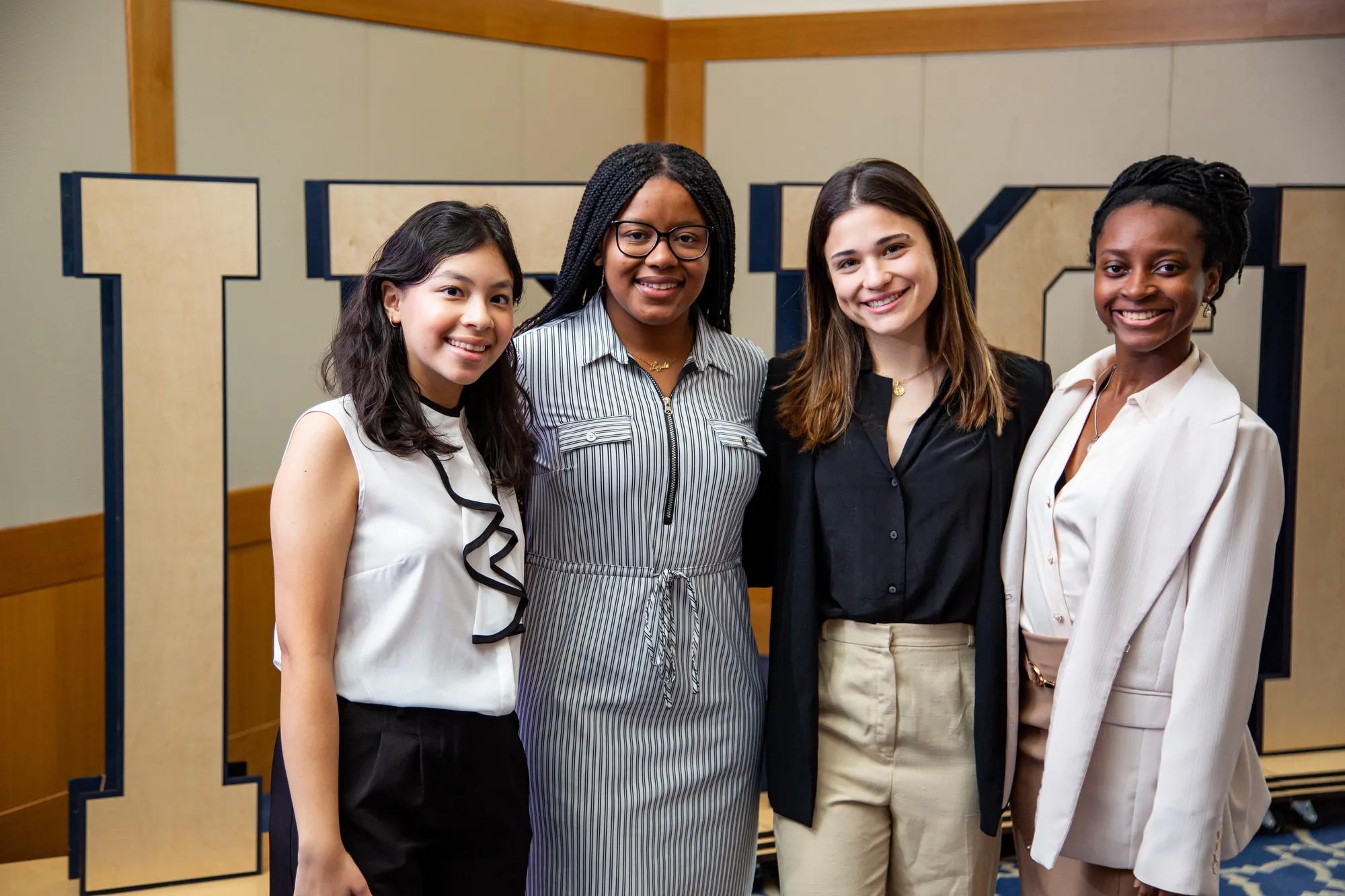 A team of four female students dressed in business professional attire pose for a photo. 