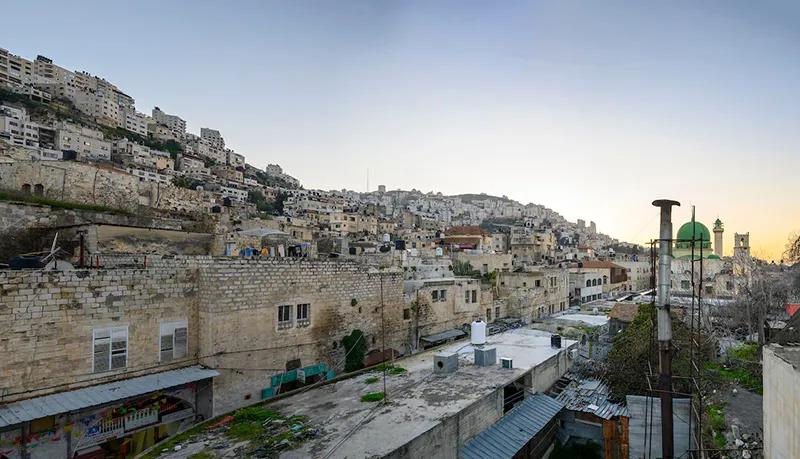 Panoramic view of a hillside in Nablus Palestine cityscape with densely packed buildings, a mosque with green domes, and a clear sky at dusk.